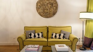 Ein gelbes Sofa mit Kissen in Schwarz und Weiß, einer runden Wanddekoration und einer Lampe auf einem Tisch.
