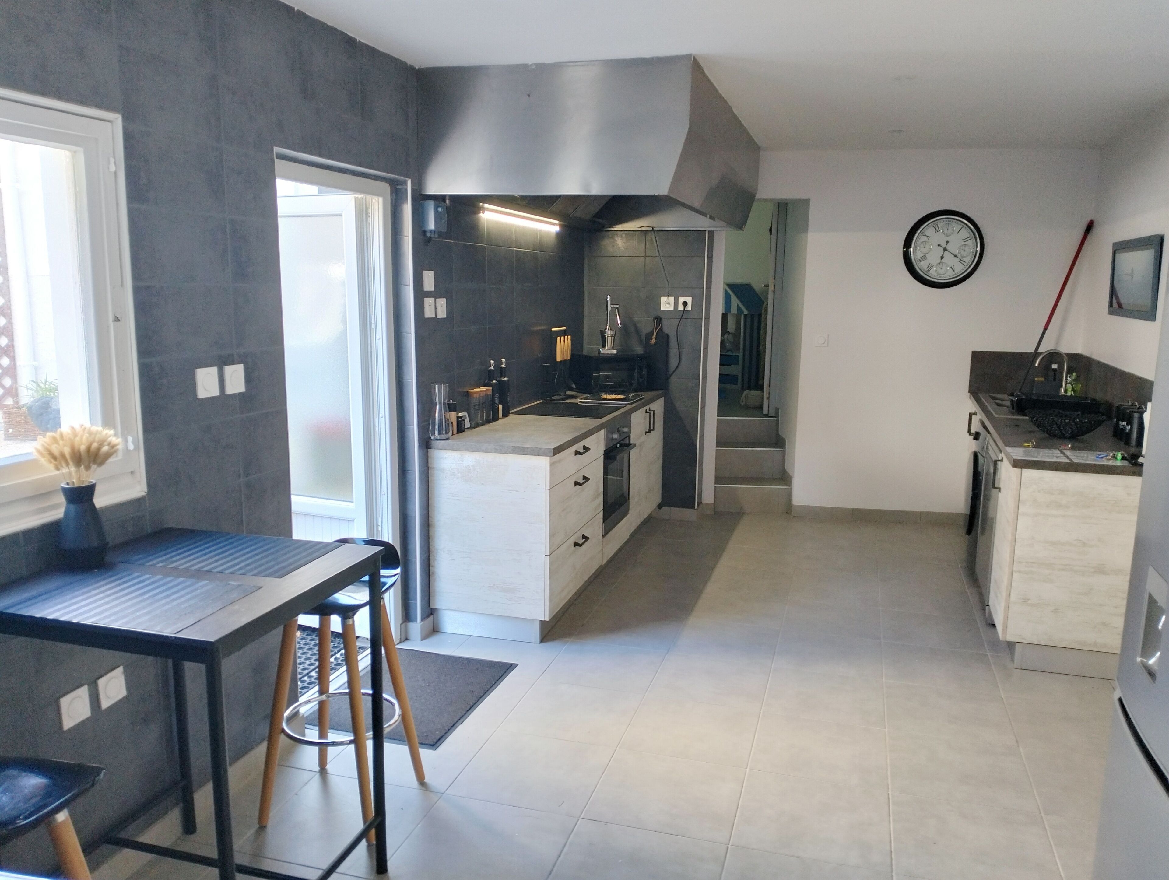 A modern kitchen with a central island, a dining area with stools, and a view of the living area through an open door.