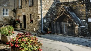A stone building with a gothic arch entrance, a small garden with red flowers, and a paved street. - Authentic 16th-century Breton house in the heart of downtown, 2 minutes from the beach (Saint-Pol-de-Léon)