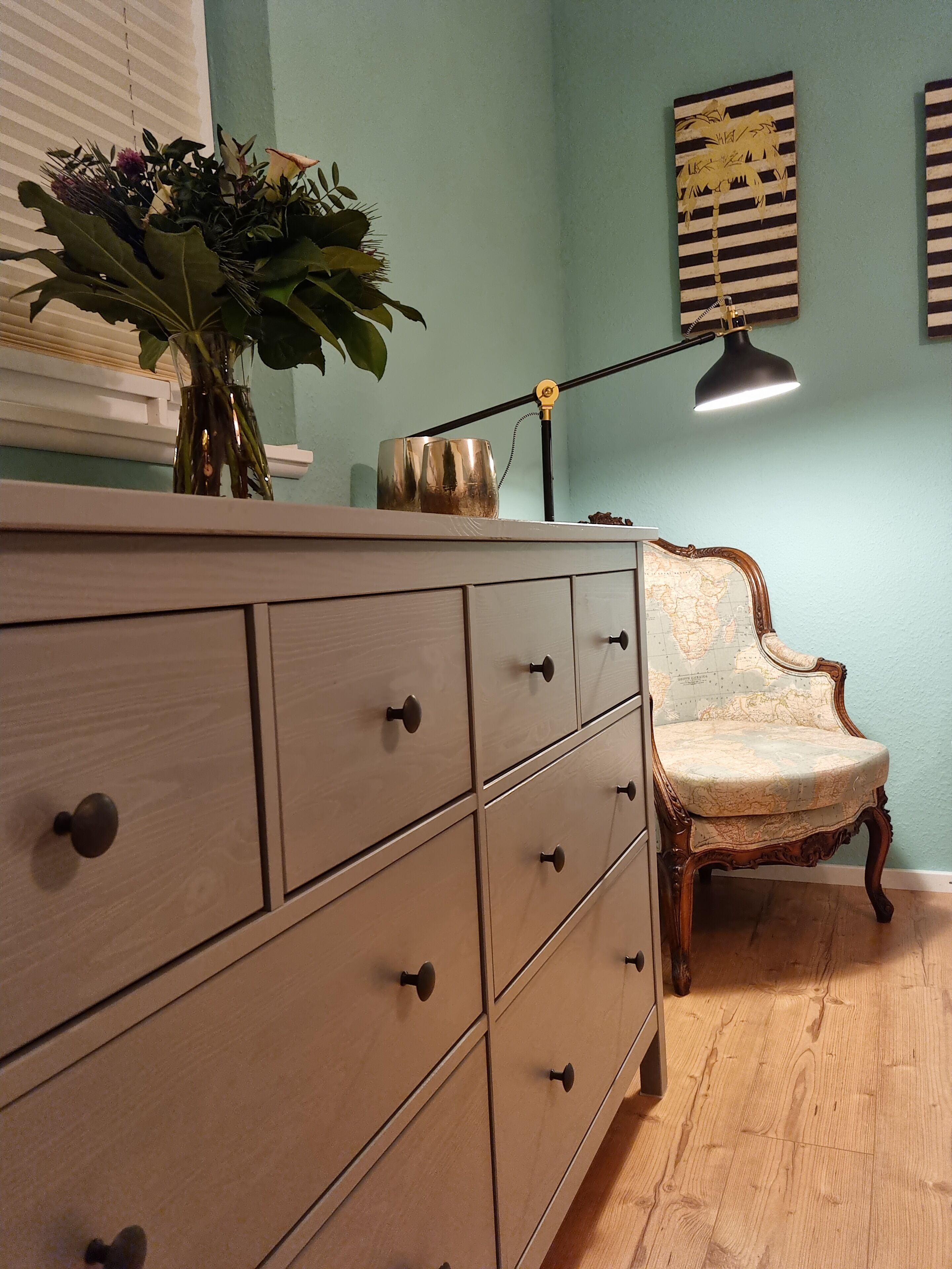 Un aparador de madera con varios cajones, un florero con una planta, un mapa terráqueo y una silla antigua.