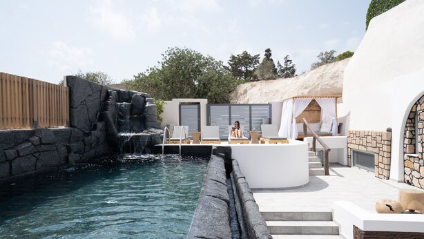 Un área de piscina con cascada, sillas de descanso y un muro de piedra.