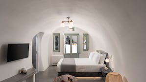 Un dormitorio moderno con una cama grande, un televisor de pantalla plana, un banco y una mesa con fruta.