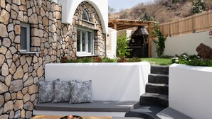 Un patio moderno al aire libre con un muro de piedra, un banco de madera y una mesa pequeña con un cuenco de fruta.