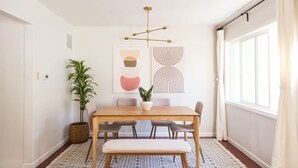 A dining area with a wooden table, bench, and chairs, a potted plant, and abstract wall art. - The Laurel Pad -12-Min From SFO, Tastefully Designed, Work Station (San Mateo)