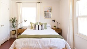 A neatly arranged bedroom with a bed, bedside tables, a lamp, and a window with curtains. - The Laurel Pad -12-Min From SFO, Tastefully Designed, Work Station (San Mateo)