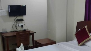 A hotel room with two beds, a desk, a television, and a purple curtain. - Magvaris Comfort Inn (Shillong)