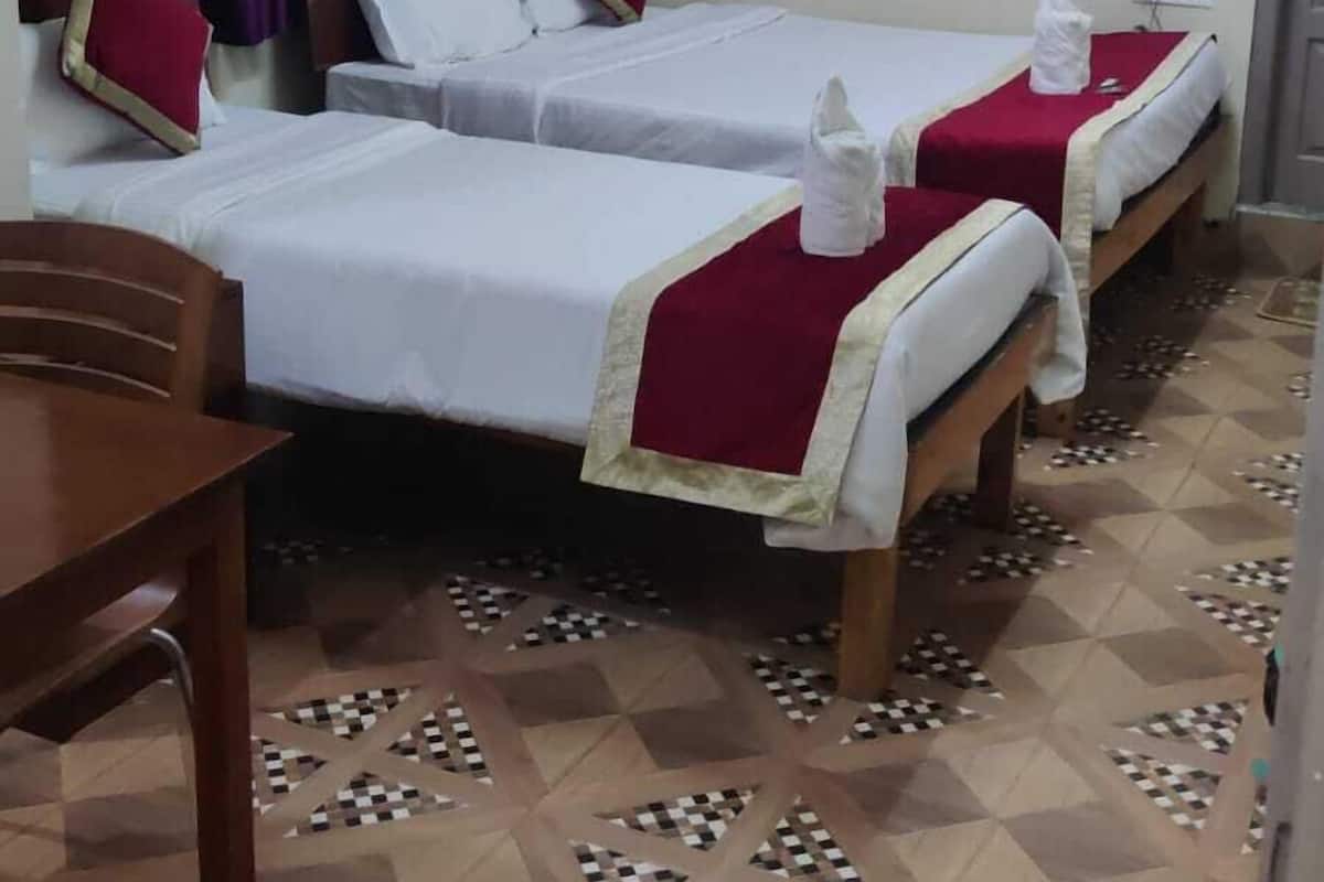 A hotel room with three beds, a wooden table, and a patterned floor.