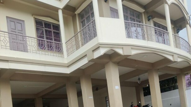 A multi-story building with a covered entrance, a balcony with a decorative railing, and a tiled floor. - Magvaris Comfort Inn (Shillong)