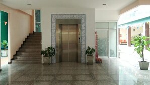 A spacious lobby with a central elevator, a staircase on the left, and potted plants. - MRT Thaphra spthaphra (Bangkok)
