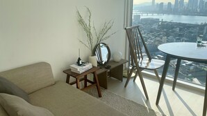 A modern living room with a sofa, a small table with books and a plant, a chair, and a view of a cityscape and river. - Amazing river view! best place to travel Seoul :) (서울특별시)