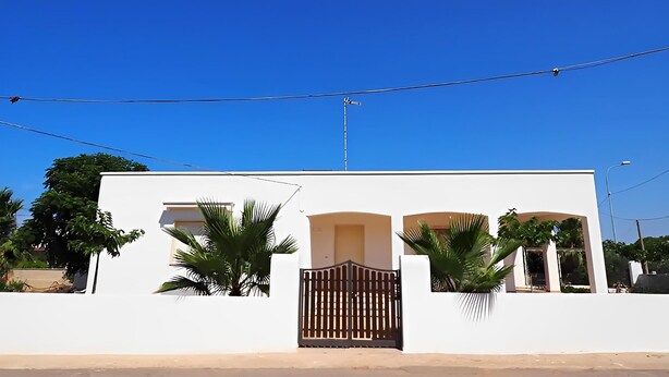 A white building with a gated entrance, palm trees, and a clear blue sky. - 3243 Villetta Morelli by Barbarhouse (Racale)