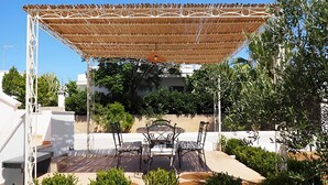 An outdoor patio with a woven canopy, a table with four chairs, and surrounding greenery. - 3243 Villetta Morelli by Barbarhouse (Racale)