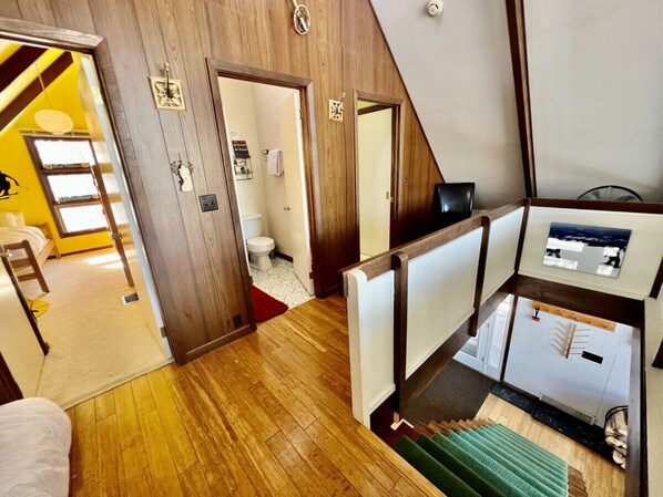 A multi-level interior with wooden floors, a staircase, a small seating area, and a view of a bathroom.