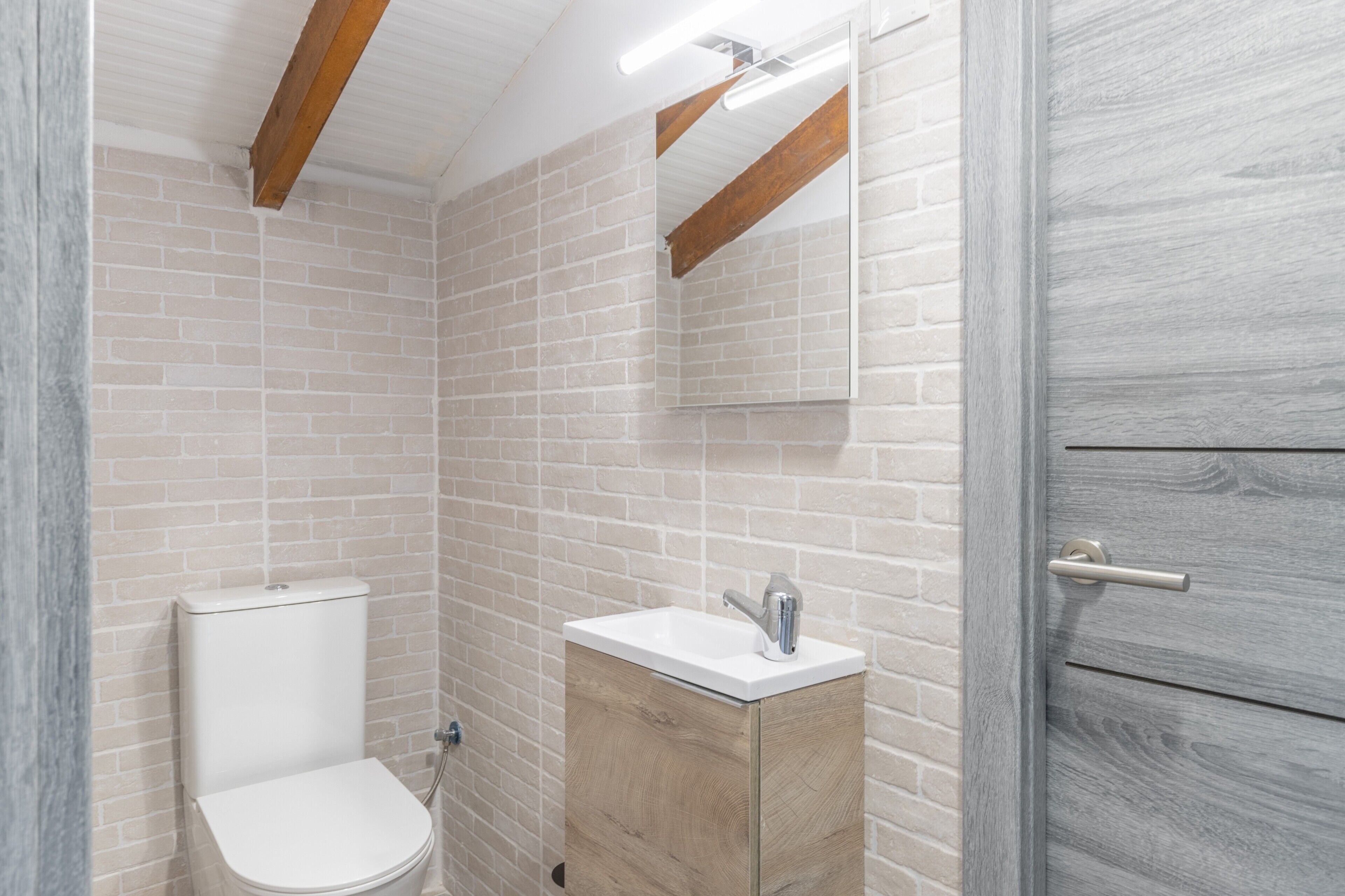 Une salle de bain avec des toilettes blanches, un meuble en bois avec un lavabo et un miroir au-dessus.