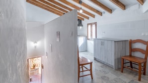 Une pièce avec un escalier, une chaise en bois, un coin cuisine avec des placards et une fenêtre.