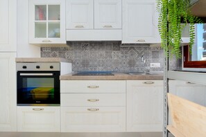 A kitchen with white cabinets, a built-in oven, a patterned backsplash, and a hanging plant.