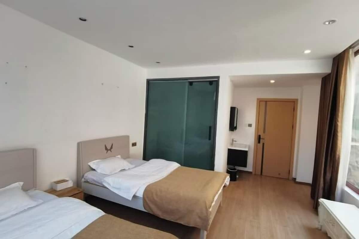 A hotel room with two beds, a wardrobe, a desk, and a window with curtains.