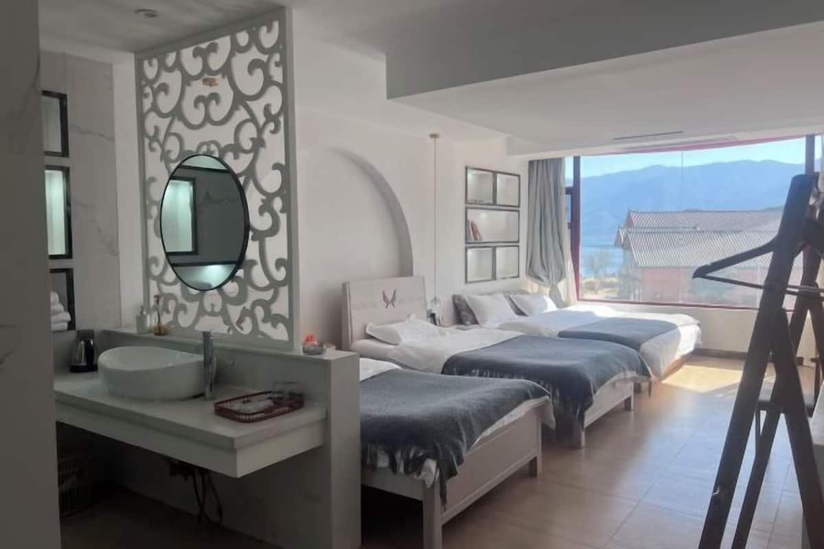 A hotel room with a large window, a bed, a bedside table, a mirror, and a bathroom with a sink and toilet.