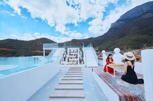 A poolside area with a clear view of mountains, a glass bridge, and a seating area with a table and chairs.