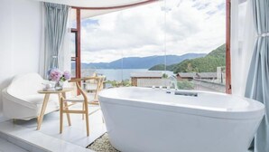 A modern bathroom with a freestanding bathtub, a white chair, and a small table with a vase of flowers. - Lugu Lake Jimei Du Nuo Wu Yun Inn (Ninglang)