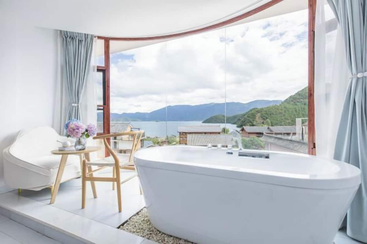 A modern bathroom with a freestanding bathtub, a white chair, and a small table with a vase of flowers.