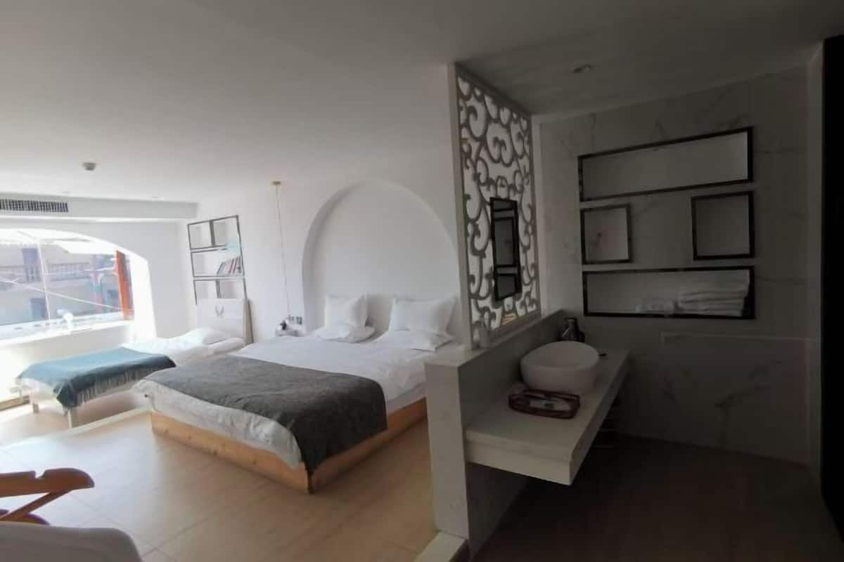 A modern hotel room with a large bed, a separate seating area, a bathroom with a vanity, and a view through the window.