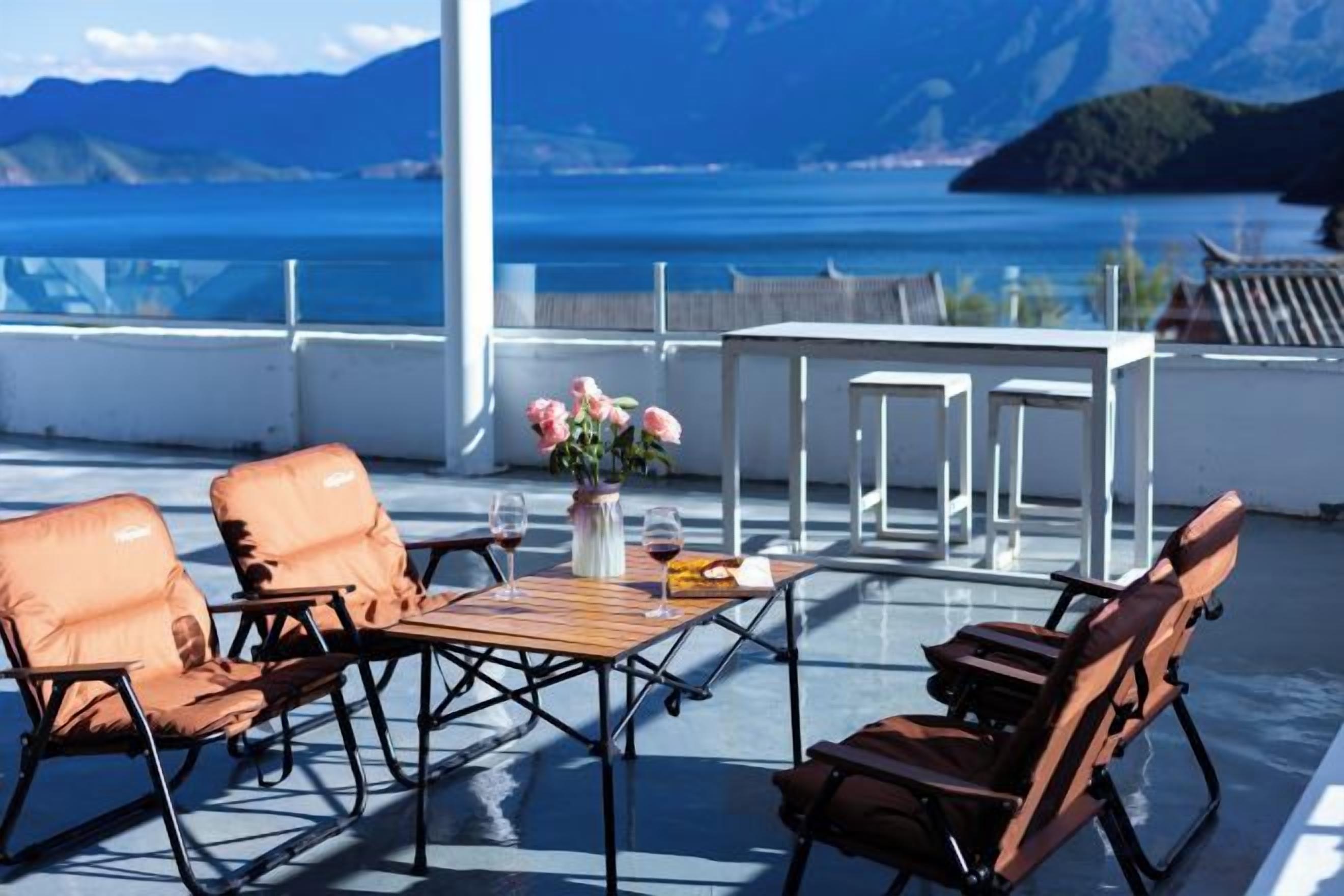 Een terras met zitplaatsen en een tafel, met uitzicht op een waterpartij en bergen.