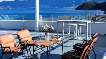 Een terras met zitplaatsen en een tafel, met uitzicht op een waterpartij en bergen.