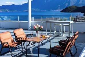 A deck with seating and a table, overlooking a body of water and mountains. - Lugu Lake Jimei Du Nuo Wu Yun Inn (Ninglang)