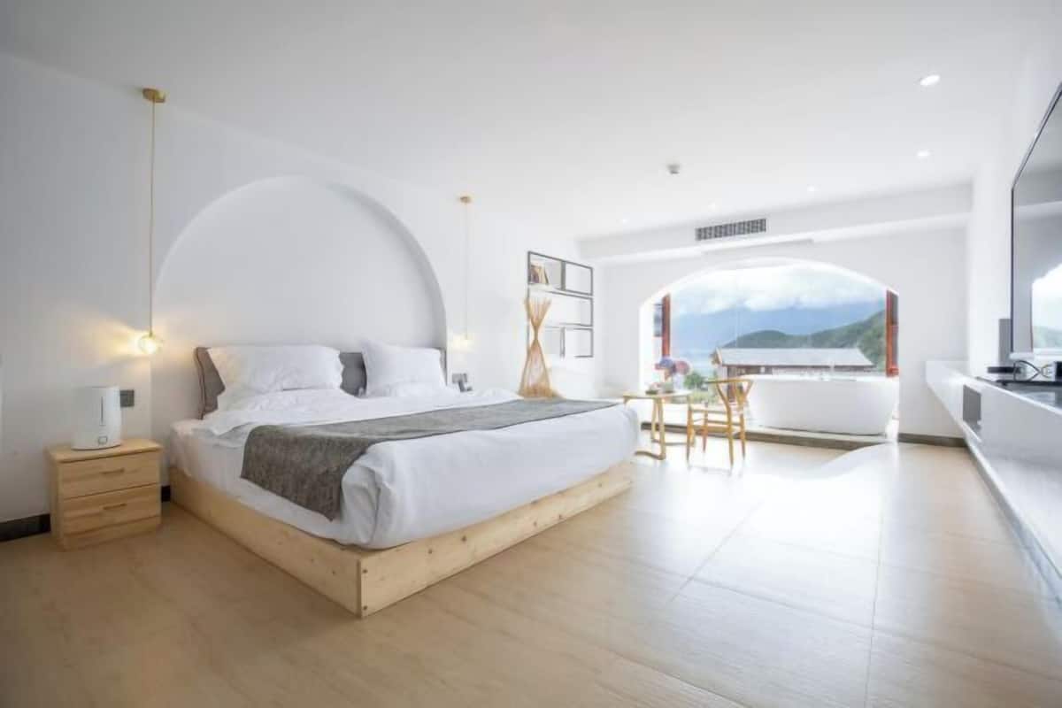 A modern bedroom with a wooden bed, bedside table, and a view of the outdoors.