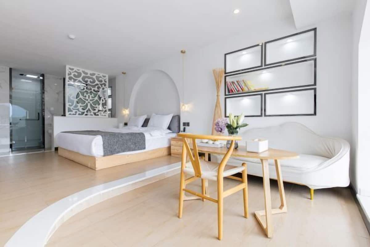 A modern hotel room with a bed, a sofa, a wooden table, and a wall with framed pictures.