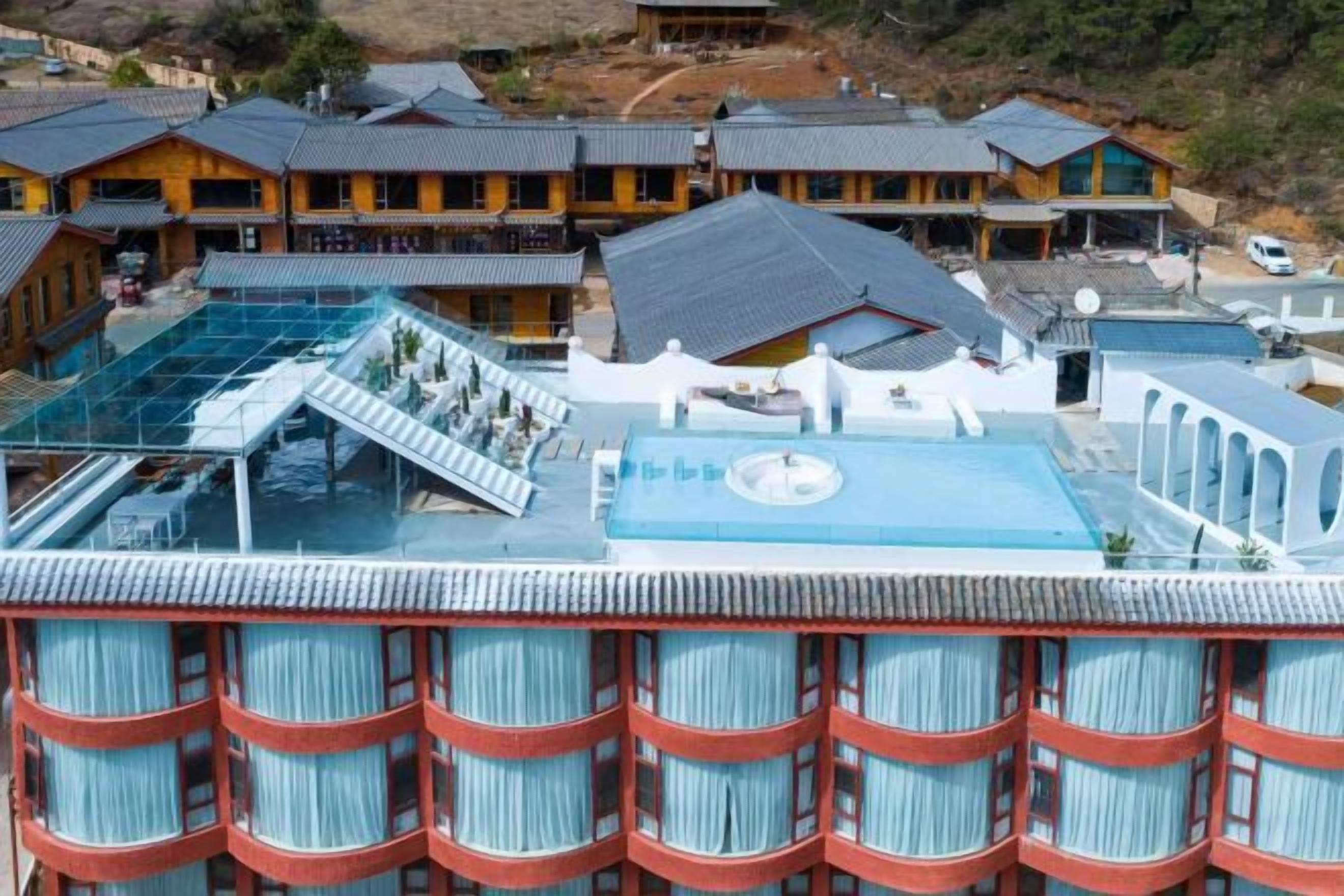 Un hotel con piscina en la azotea, varios balcones y un edificio grande con techo inclinado.