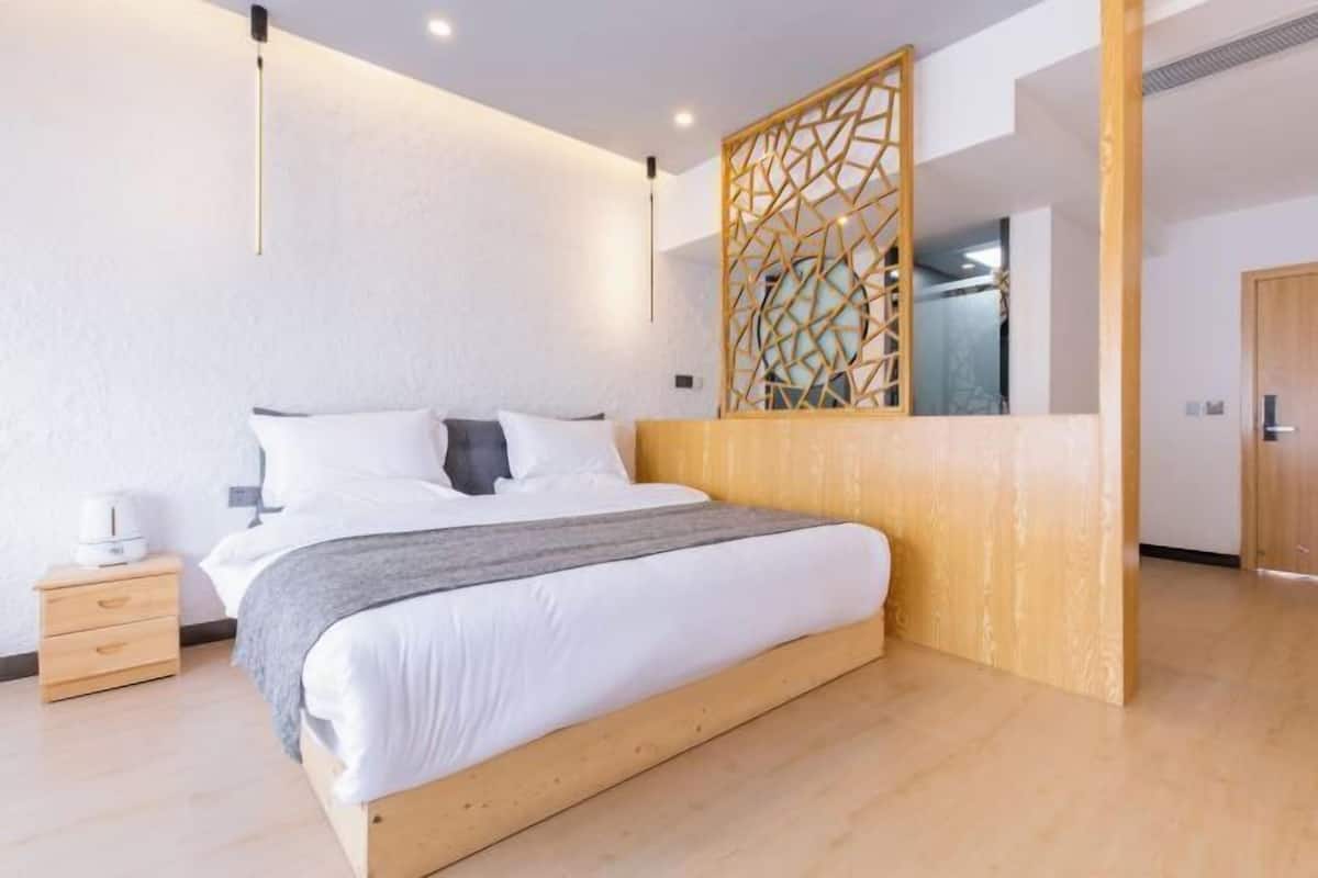 A modern bedroom with a wooden bed frame, a nightstand, a decorative wall panel, and a wooden door.