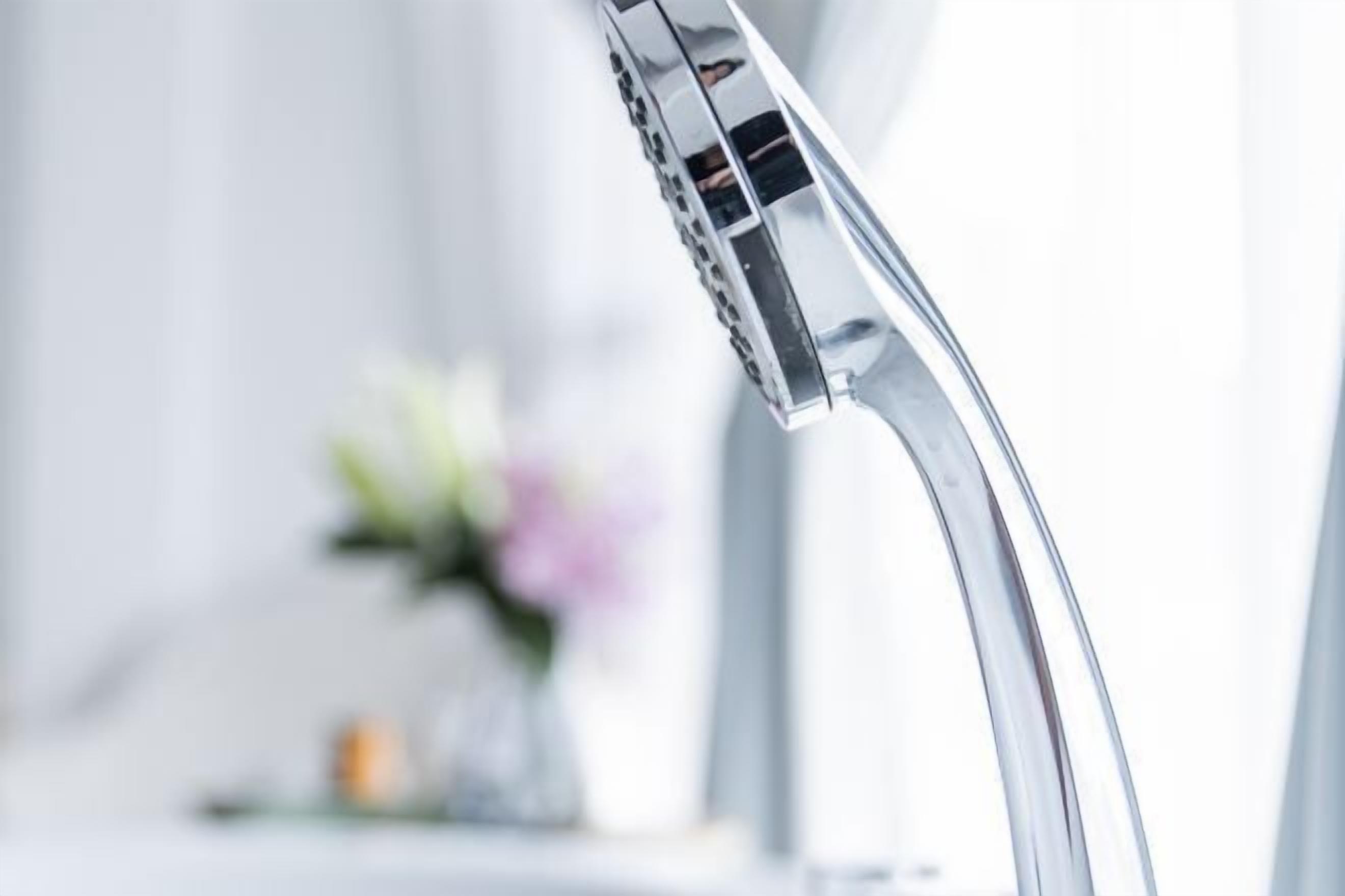 A modern bathroom with a chrome faucet and a vase with flowers in the background.