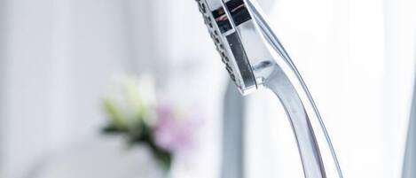 A modern bathroom with a chrome faucet and a vase with flowers in the background.