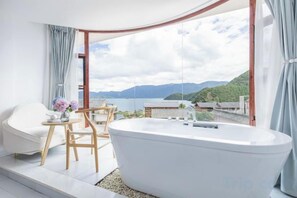 Un baño moderno con una bañera independiente, un rincón de estar con mesa y sillas, y un amplio ventanal con vistas a las montañas.
