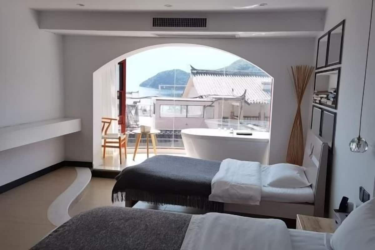 A modern hotel room with a large arched window, a bed, a small table, and a view of a traditional building.