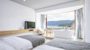 A modern hotel room with two beds, a TV, a balcony with a view of the sea, and a bathtub.