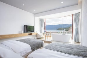 Una habitación de hotel moderna con dos camas, televisor, balcón con vistas al mar y bañera.