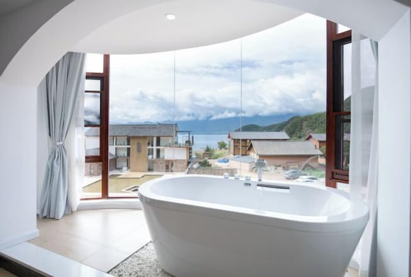 Un baño moderno con una bañera independiente, ventanas amplias y vistas a un paisaje costero.