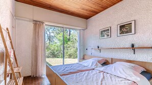 A bedroom with a bed, wooden ladder, and a large window with curtains.