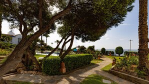 A stone pathway leading through a landscaped garden with trees and a view of the sea. - Apartment "La Perla de Marakech 5" with Sea View, Shared Pool & Wi-Fi (Casares)
