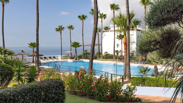 A pool area with palm trees, a white building, and a view of the sea. - Apartment "La Perla de Marakech 5" with Sea View, Shared Pool & Wi-Fi (Casares)