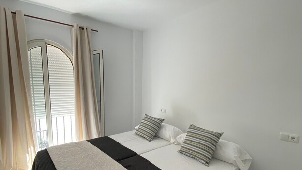 A bedroom with a bed, two pillows, a window with curtains, and a ceiling light.