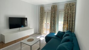 A modern living room with a flat-screen TV, a white sofa, a coffee table, and patterned curtains.