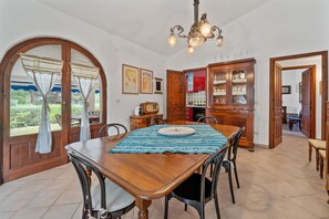 A dining area with a wooden table, chairs, a chandelier, and a view through an arched doorway.
