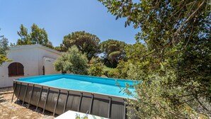 Una piscina amb un solàrium cobert, una taula amb begudes i un edifici petit al fons.