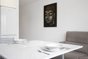 Uma sala de jantar moderna com uma mesa branca posta para dois, um sofá cinza e uma pintura de Buda na parede.