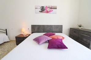 A neatly made bed with pillows, a bedside lamp, a nightstand, a dresser, and a wall-mounted picture. - Holiday Home "Casa Giorgia in Otranto 8 Guests" with Balcony & A/C (Otranto)