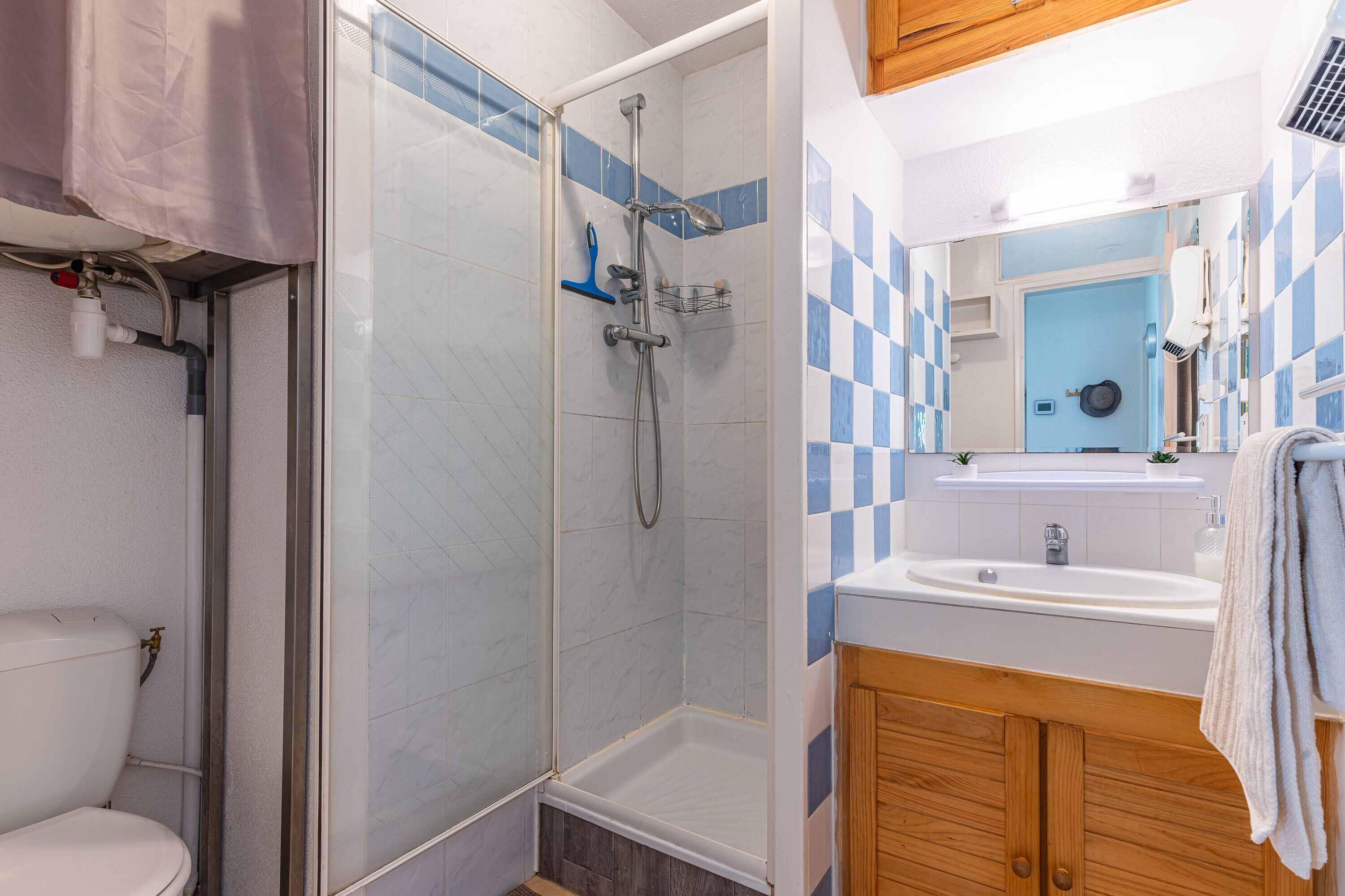 Un baño con ducha acristalada, inodoro, lavabo y armarios de madera.